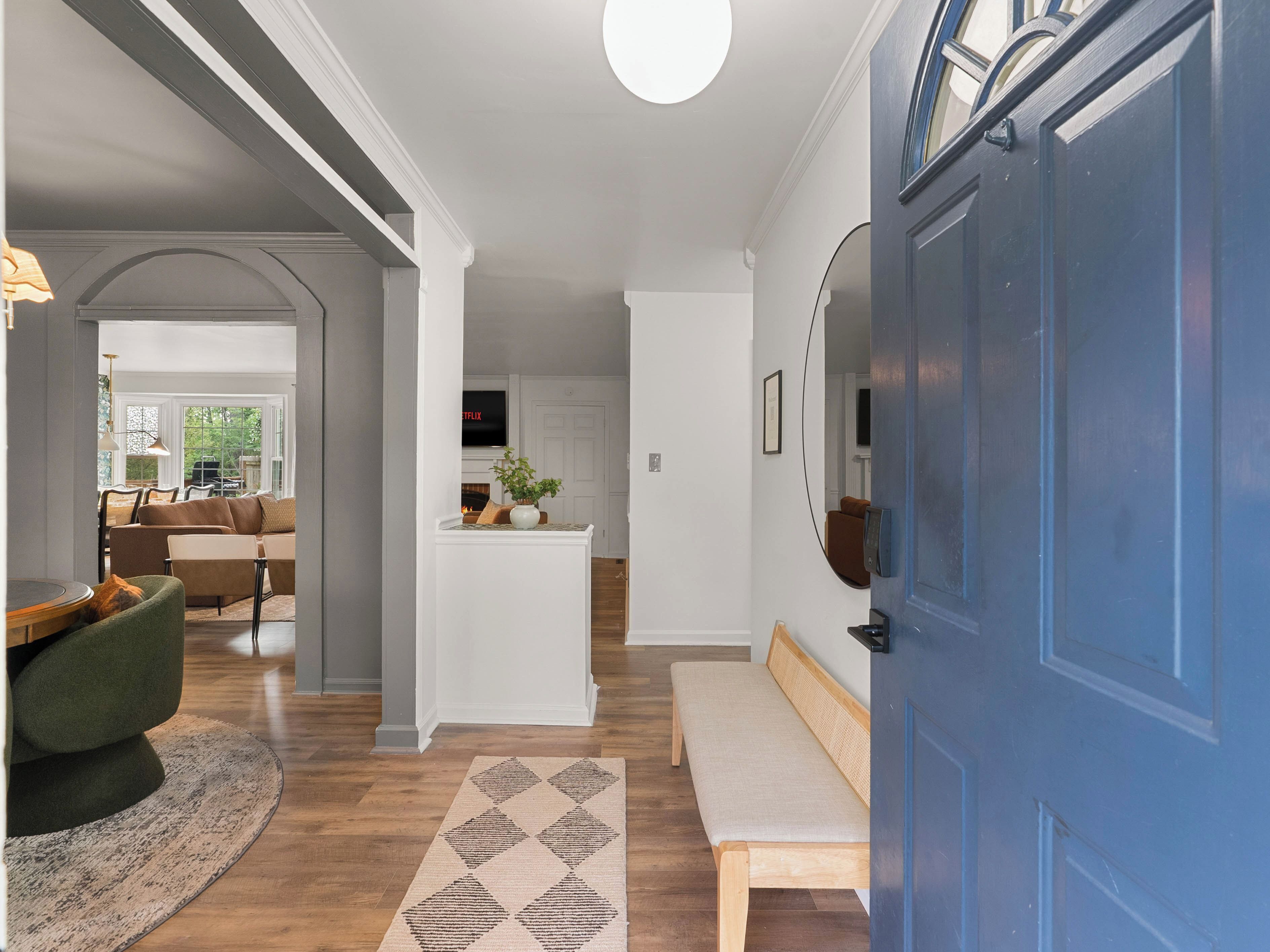 Un intérieur moderne avec un plancher en bois, une porte bleue, un banc, une console blanche et un téléviseur fixé au mur.