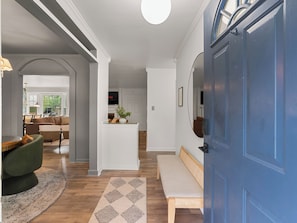 A modern interior with a wooden floor, a blue door, a bench, a white console table, and a TV mounted on the wall.