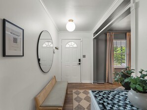 Un couloir avec un banc, un panneau d’accueil encadré, un miroir et une porte.