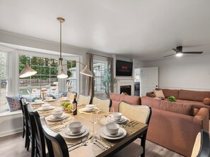 Un comedor con una mesa larga dispuesta para seis personas, un sofá y un televisor sobre la chimenea.
