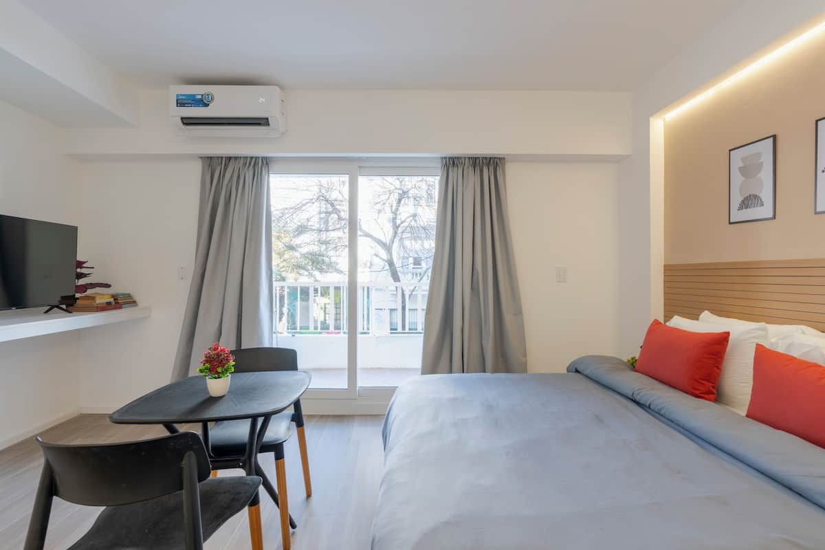 Ein Hotelzimmer mit Bett, Fernseher, einem kleinen Tisch mit Pflanze und Balkonblick.
