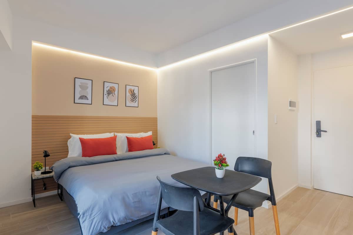 Ein modernes Schlafzimmer mit Bett, Nachttisch, Lampe und einem kleinen Tisch mit Stuhl.