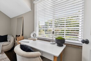 A modern room with a white desk, a chair, a large mirror, and a window with white blinds. - Modern 2BR Broadleigh Gem, Bright & Stylish (Columbus)