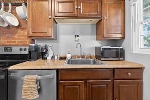 A kitchen with wooden cabinets, a stainless steel sink, a microwave, and a stove. - Modern 2BR Broadleigh Gem, Bright & Stylish (Columbus)