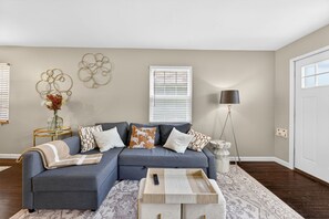 A living room with a sectional sofa, a side table with a vase, a floor lamp, and a patterned rug. - Modern 2BR Broadleigh Gem, Bright & Stylish (Columbus)