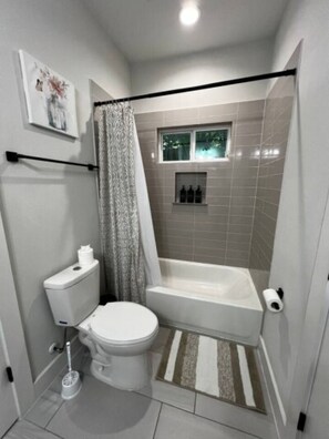 Une salle de bain moderne équipée de toilettes, d’une douche et d’une fenêtre située au-dessus de la douche.