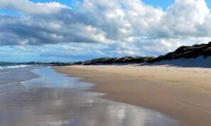 A beach with a wide sandy shore, gentle waves, and a partly cloudy sky.