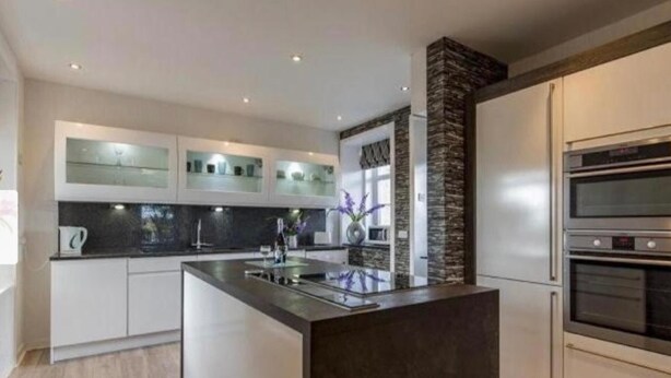 Uma cozinha moderna com uma ilha central, eletrodomésticos embutidos e uma parede decorada com pedra.