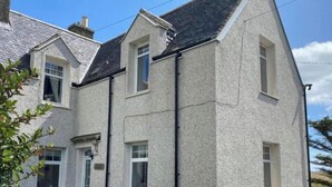 Uma casa de dois andares com telhado inclinado, várias janelas e uma chaminé visível.