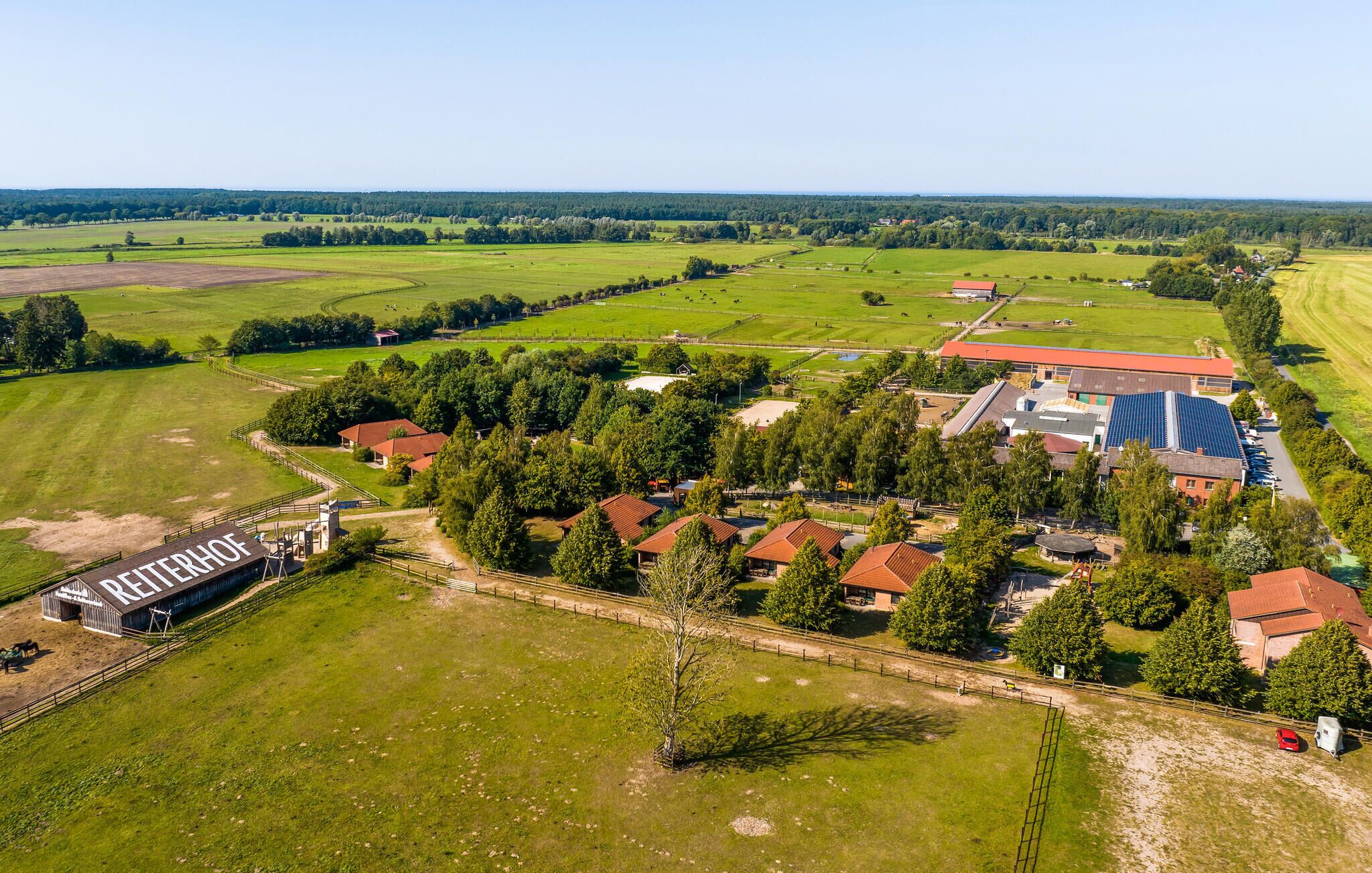 An aerial view of a rural property with a large barn labeled 'REITERHOF,' surrounded by green fields and scattered trees.