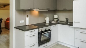 Een moderne keuken met grijze kastjes, een zwart aanrecht, een inbouwoven en een koffiezetapparaat.