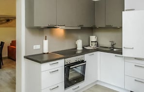Eine moderne Küche mit grauen Schränken, einer schwarzen Arbeitsplatte, einem eingebauten Ofen und einer Kaffeemaschine.