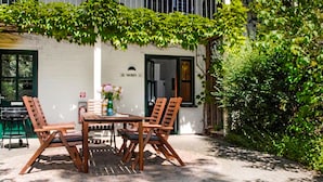 An outdoor patio with a table and four wooden chairs, a vase with flowers, and a bottle of water. - Beautiful apartment in Ribnitz-Damgarten with house a panoramic view (Ribnitz-Damgarten)