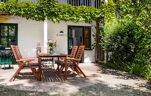 Eine Terrasse im Freien mit einem Tisch, vier Holzstühlen, einer Blumenvase und einer Wasserflasche.