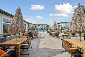 Eine Terrasse mit Tischen und Stühlen, ein Schwimmbad und Gebäude im Hintergrund.