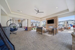 A spacious outdoor lounge area with seating, a hanging chair, and a flat-screen TV mounted on a brick wall.