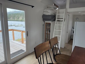 Et værelse med en skydedør til en træterrasse, et loft med opbevaring, et tekøkken og udsigt til en sø.