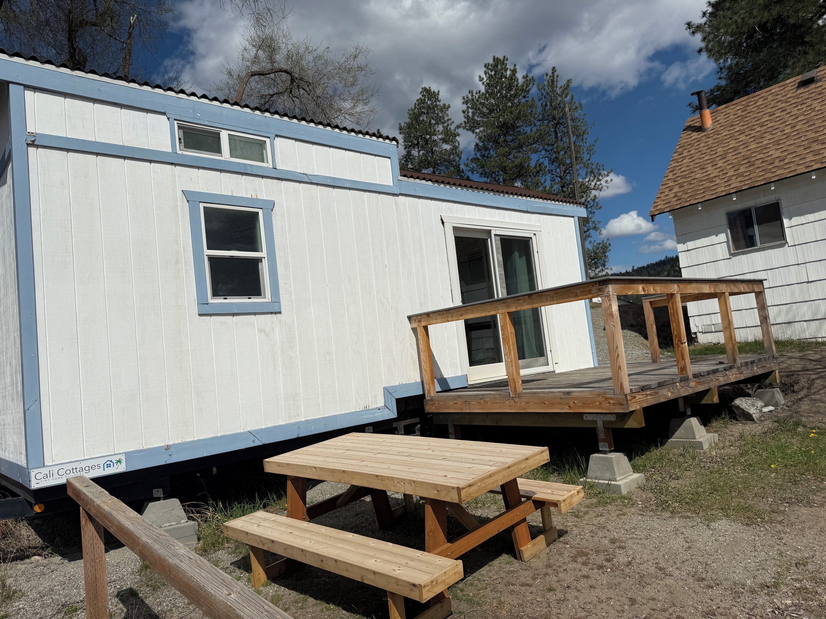 A mobile home with a deck, picnic table, and a sign indicating 'Cali Cottages.'