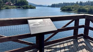 Terraza de madera con vista a un lago y un cartel.
