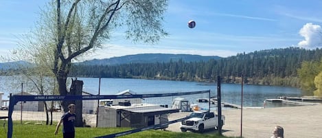 A volleyball game in a park with a lake and mountains in the background.