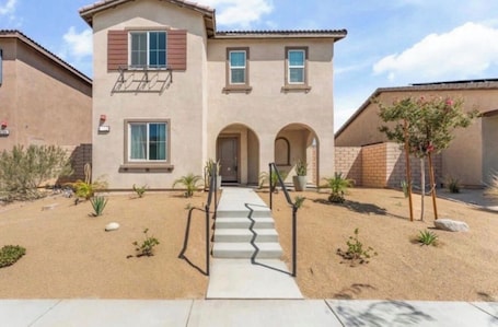A two-story house with a front entrance, a small patio, and a staircase leading to the door.. Verano Gateway