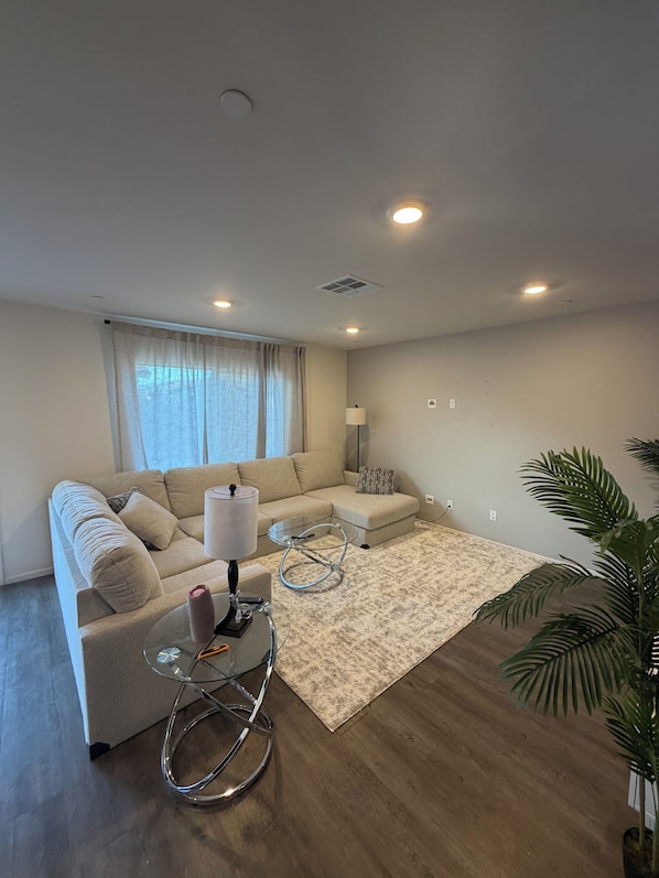 A modern living room with a sofa, a glass coffee table, a lamp, and a potted plant.