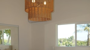 Een slaapkamer met een groot bed, een nachtkastje, een lamp, een spiegel en een raam met uitzicht op groen.