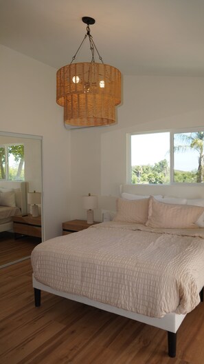 A bedroom with a large bed, a bedside table, a lamp, a mirror, and a window with a view of greenery. - 4-bedroom ranch house in peaceful Malibu with ocean and mountains view (Malibu)