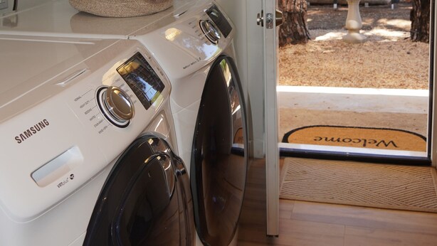 Wasruimte met een Samsung wasmachine, een droogrek en een deur naar een buitenruimte met een welkomstmat.