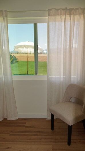 Een kamer met een raam, een stoel en uitzicht op een veld.