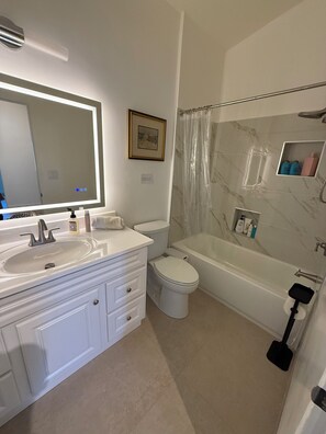 Et badeværelse med vask, spejl, toilet, badekar og bruseforhæng.
