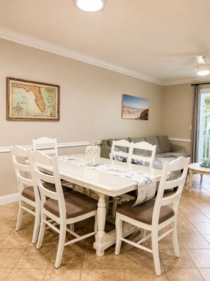 Un coin repas avec une table et des chaises blanches, une carte accrochée au mur et un tableau.