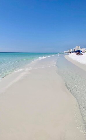 Une plage avec une eau cristalline, un rivage sablonneux et des bâtiments en arrière-plan.