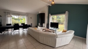 Ein modernes Wohnzimmer mit einem weißen Sofa, einem Esstisch, Stühlen, einem Fernseher und einem Kamin.