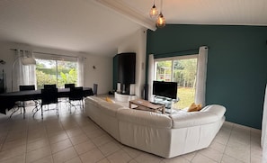Ein modernes Wohnzimmer mit einem weißen Sofa, einem Esstisch, Stühlen, einem Fernseher und einem Kamin.