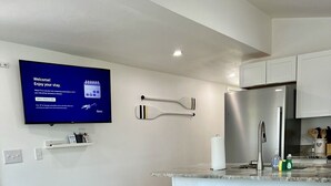 Una cocina moderna con una televisión de pantalla plana, taburetes de bar blancos, un sofá gris y una mesa de centro de madera.