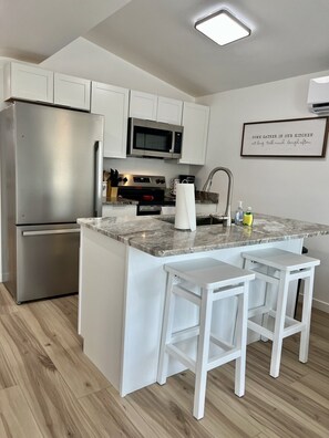 A modern kitchen with a stainless steel refrigerator, a microwave, and a built-in oven. There are two white bar stools and a marble countertop. - GOTL- Sun Retreats/Heated Pool/Free Golf Cart (Geneva)