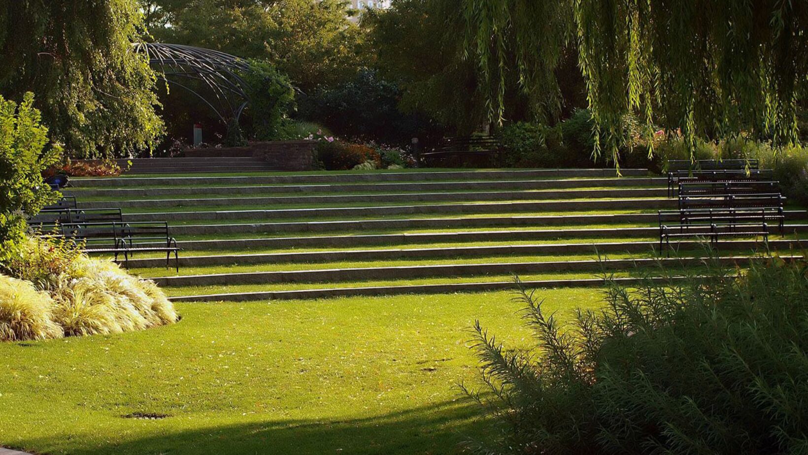 A park with a series of steps leading up to a structure, surrounded by greenery and trees.