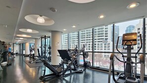 Ein Fitnessstudio mit Trainingsgeräten, großen Fenstern und Blick auf Gebäude.