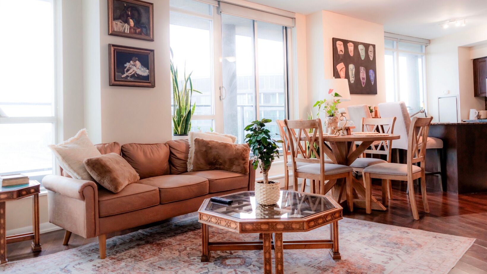 Una sala de estar con un sofá marrón, una mesa de centro de vidrio, sillas de madera, una mesa de comedor y una zona de cocina.