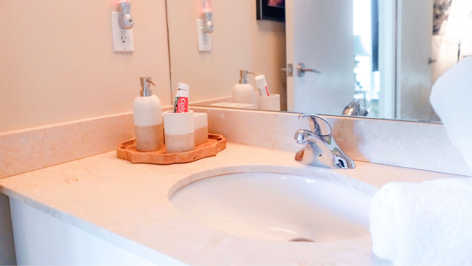 A bathroom with a sink, a mirror, and toiletries on a tray.
