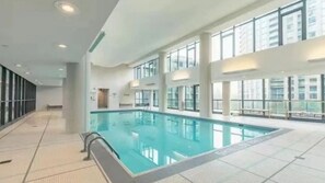 A large indoor swimming pool with clear glass walls, a tiled floor, and a high ceiling. -  3BR Penthouse Downtown & Lakeview by CN Tower- Pool, Gym, Parking (Toronto)