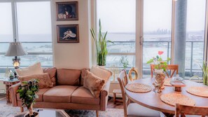 Una sala de estar con sofá, mesa de comedor, sillas, lámpara y vista de la ciudad.