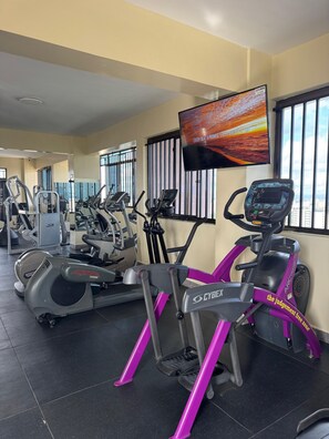 Ein Fitnessraum mit Fahrrädern, Laufbändern und einem Fernseher, der eine motivierende Meldung anzeigt.
