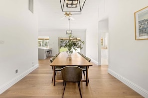 A dining area with a long wooden table, chairs, a ceiling fan, and a hanging light fixture.