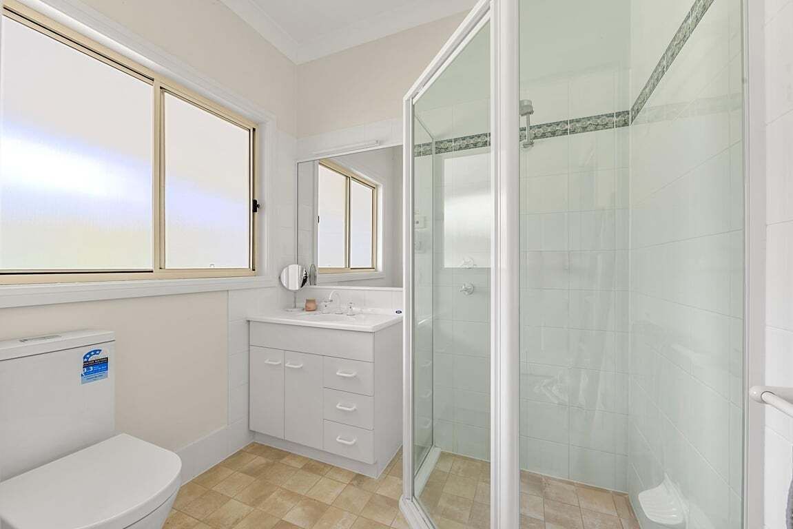 A bathroom with a toilet, a sink, a mirror, and a glass-enclosed shower.