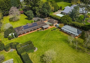 An aerial view of a residential property with a large lawn, solar panels on the roof, and a well-maintained garden.