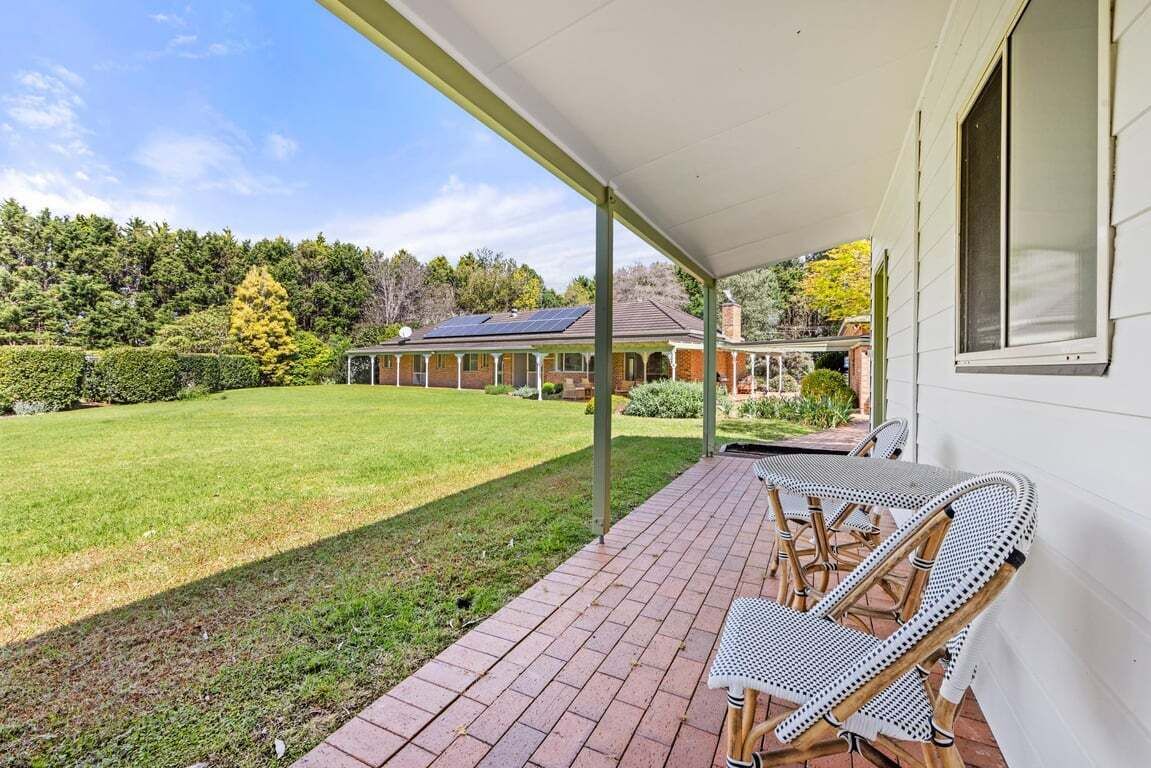 A covered patio with a table and chairs, a brick pathway, and a view of a house with a solar panel.