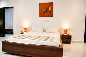 Une chambre à coucher moderne avec un lit en bois, une literie blanche, deux lampes de chevet et une œuvre d’art accrochée au mur.