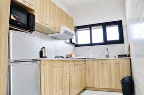 Une cuisine compacte équipée d’un réfrigérateur, d’un four à micro-ondes, d’une cuisinière et de meubles de rangement en bois.
